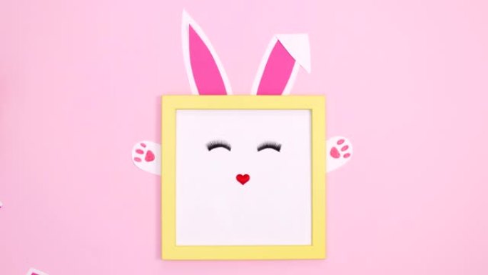 可爱的创意兔子在黄色框架，耳朵，爪子和粉红色背景上闪烁的睫毛。停止运动平铺