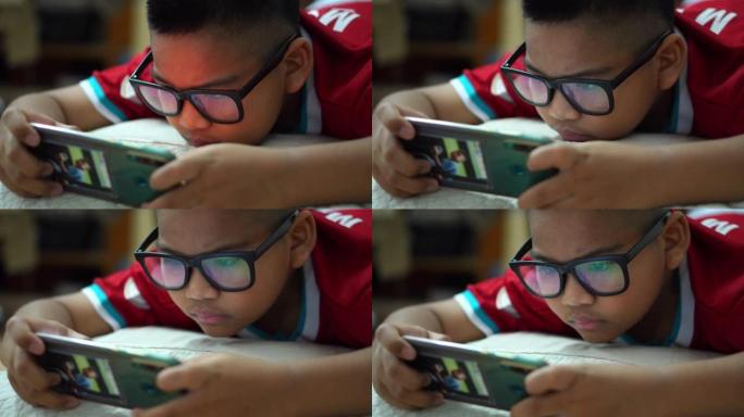 一个戴眼镜的男孩用智能手机玩游戏娱乐。