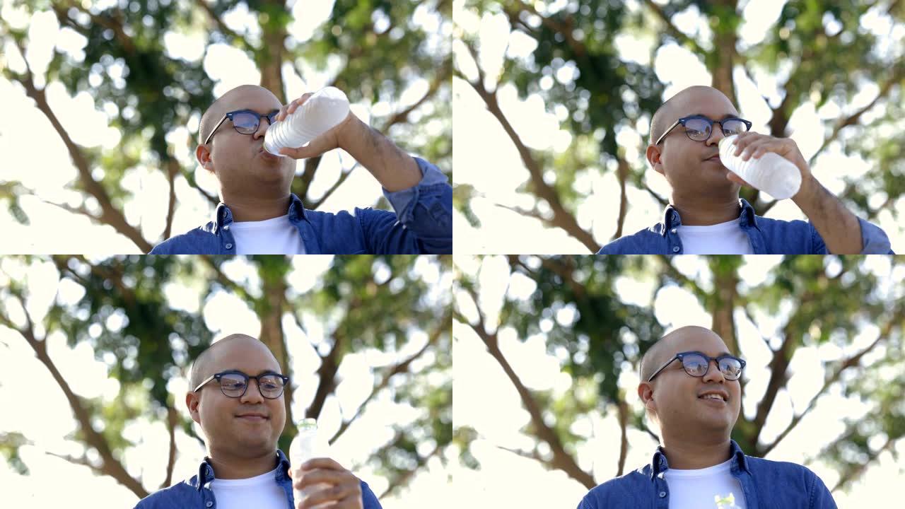 亚洲年轻人在公园里喝一瓶水的凉水。