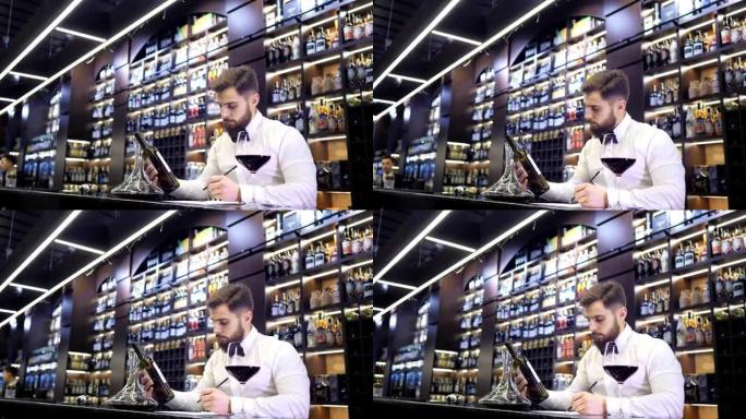 酒窖。英俊的侍酒师品尝红酒并在品尝卡上做笔记