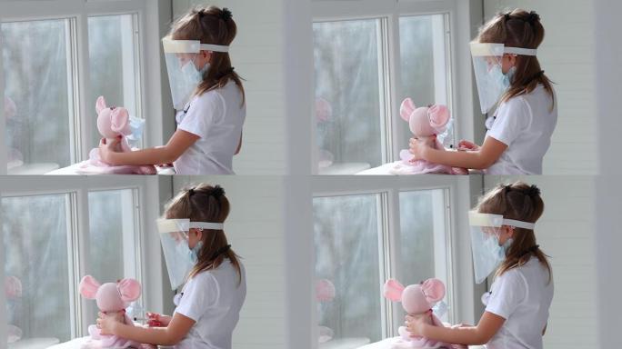 一个戴着医用口罩的可爱的小女孩拿着注射器，一边对着新型冠状病毒肺炎冠状病毒给玩具接种疫苗。聪明的孩子