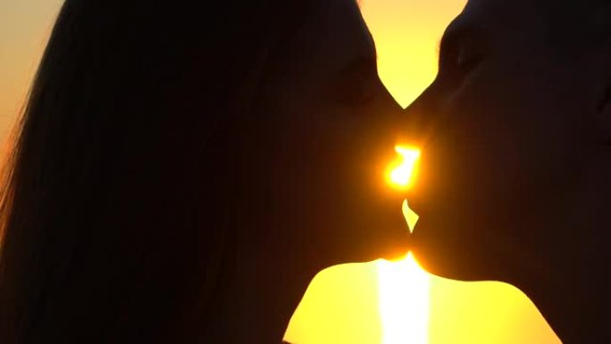 年轻浪漫情侣的剪影，两个恋人，年轻男女在海洋接吻，海上日落