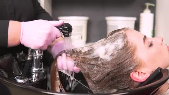 戴着手套的美发师在脸盆中洗掉客户头发上的洗发水