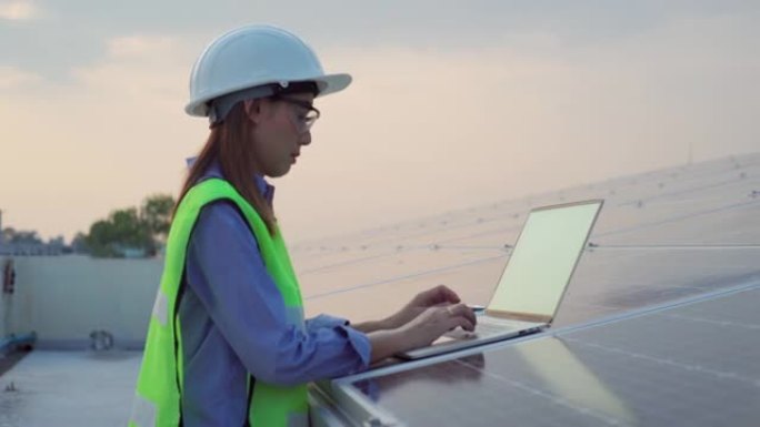 穿着制服的亚洲女工程师在太阳能电池板工厂与笔记本电脑一起工作