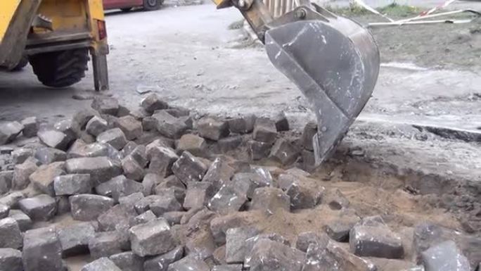 挖掘机用铲斗清除道路上的旧铺路石