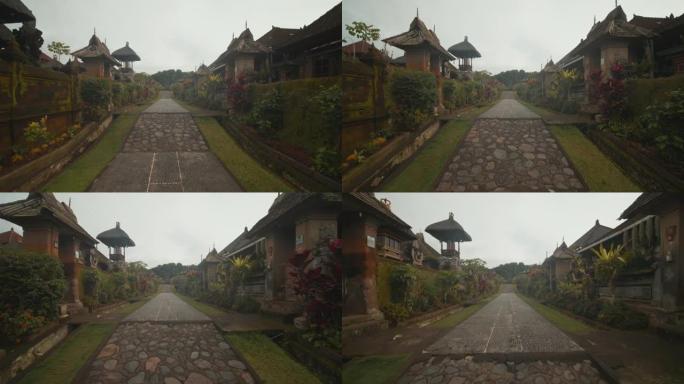 在印度尼西亚巴厘岛的传统彭利普兰村庄中沿着鹅卵石小径行走的慢速多莉视图，带有传统房屋的古老村庄的街景
