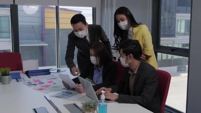 一名亚裔女员工正在向上司寻求工作计划方面的建议。团队中的每个人都戴着口罩，以防止新型冠状病毒肺炎病毒