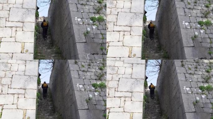 春日背景带背包的游客走上高墙之间的石阶，蓝天下有绿色植物