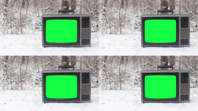 冬季积雪覆盖的地面上带有绿色屏幕的老式电视