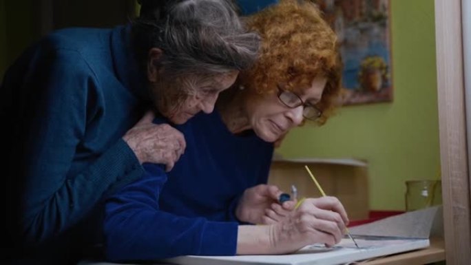 一位老母亲去养老院。在艺术工作室与一个年迈的女儿和资深母亲一起绘画课程。两个女性在画布上绘画的共同家