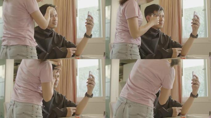 亚洲夫妇在冠状病毒大流行后在家理发，使用智能手机检查并学习在家理发。