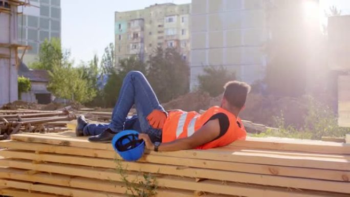 在一个建筑工地，美国黑人在休息时间在外面的树林里小睡一会儿，他醒来时戴上安全帽去上班