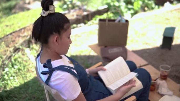 女孩坐在花园里的椅子上看书。