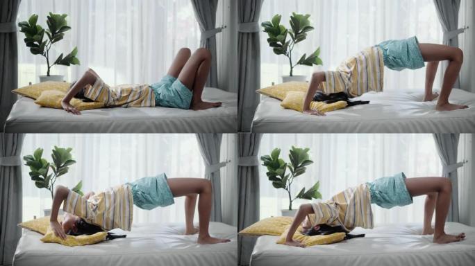 快乐的亚洲女孩在家靠窗的沙发床上桥位置做瑜伽，生活方式理念。