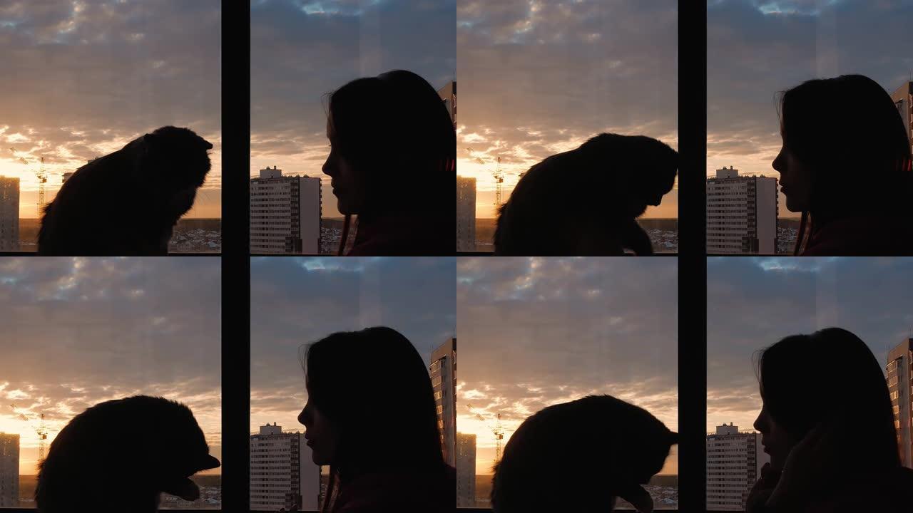 剪影一名年轻女子在夕阳的阳光下，戴着耳机在阳台上的彩色玻璃窗旁听音乐。猫洗，舔爪子