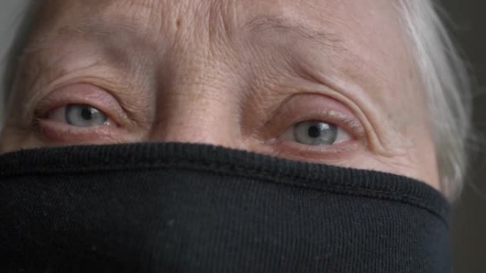 一个老妇人的眼睛被一个保护性的黑色面具遮住了一张脸。检疫。绝望。将框架从模糊到清晰度聚焦在眼睛上