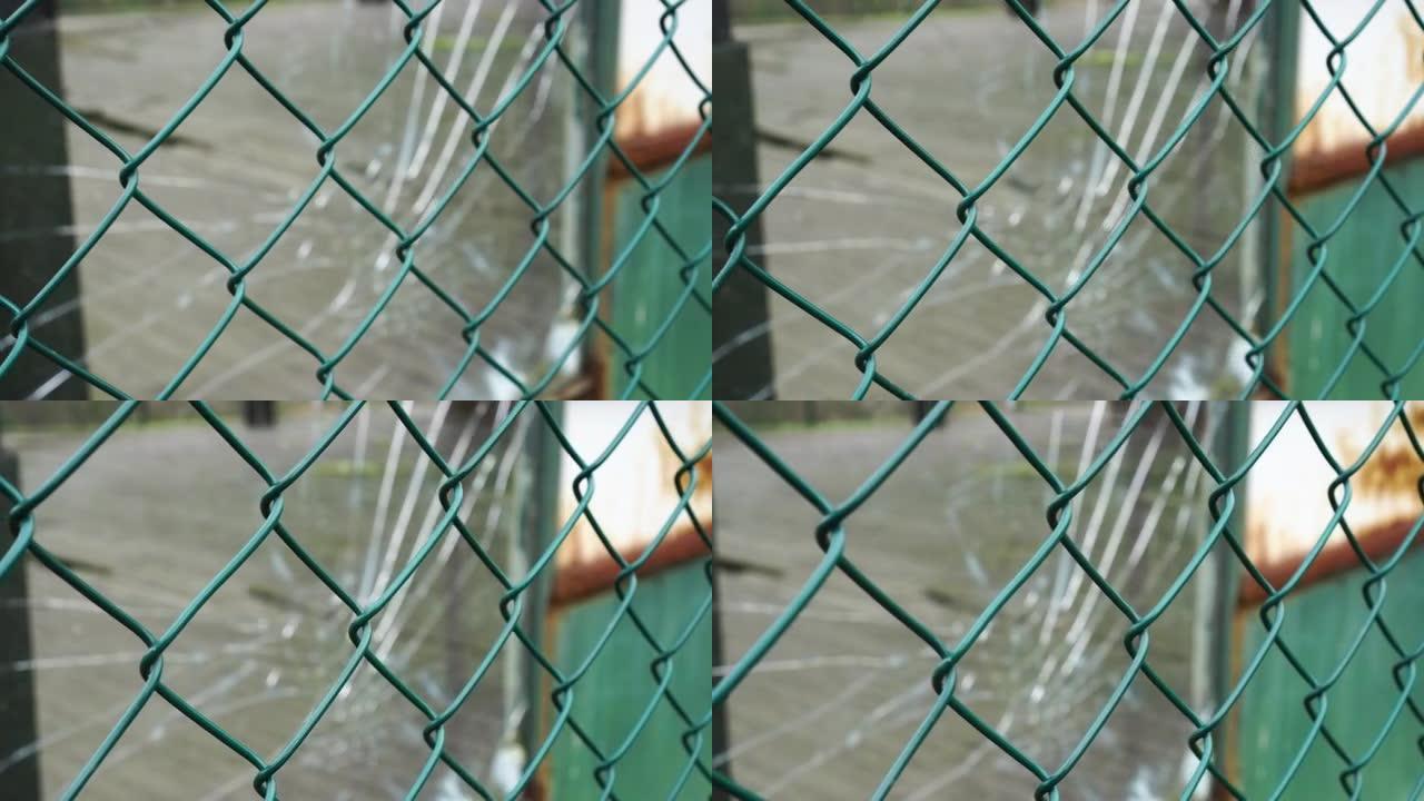 栅栏网和生锈的铁壁上的破碎玻璃窗