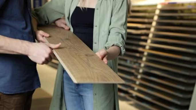 年轻夫妇在地板商店选择木质纹理层压地板进行家庭维修