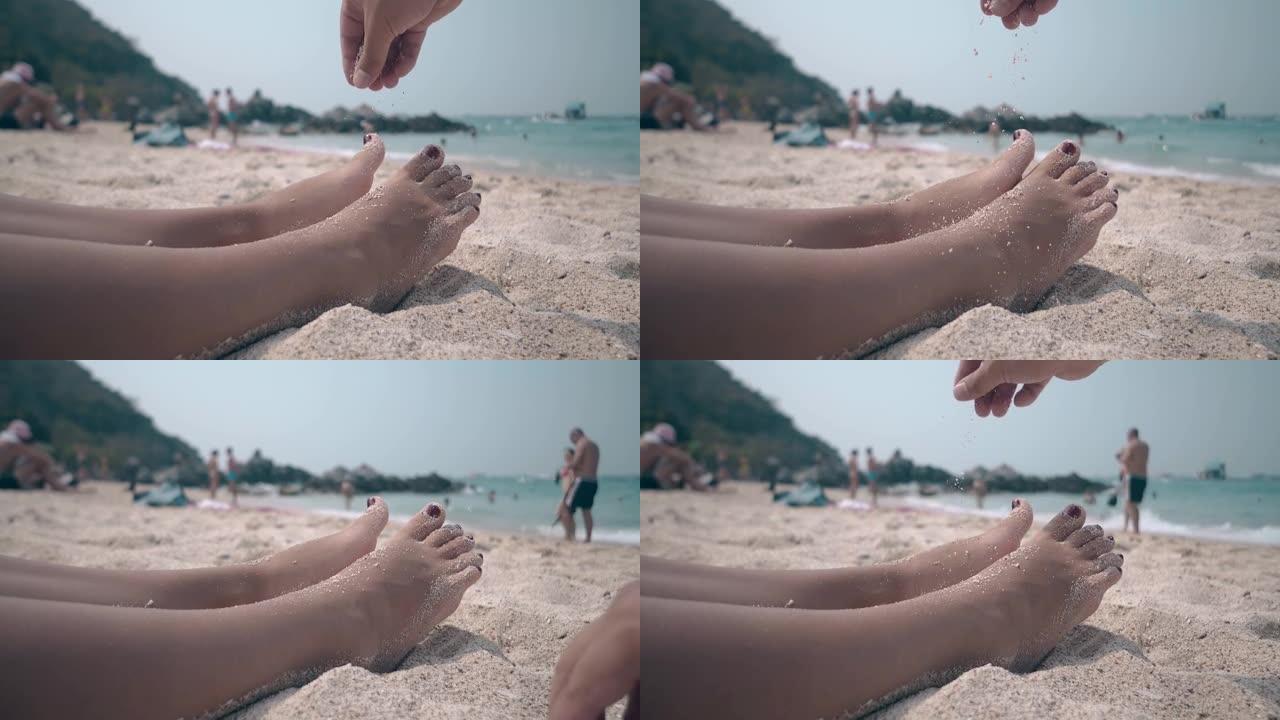 男人往躺在沙滩上的女人腿上撒一小撮沙子