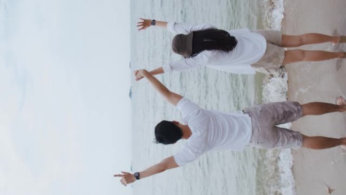 垂直视频: 恋爱中的亚洲夫妇在假期周末举起双臂庆祝成功。浪漫情侣在海滩度假旅行。