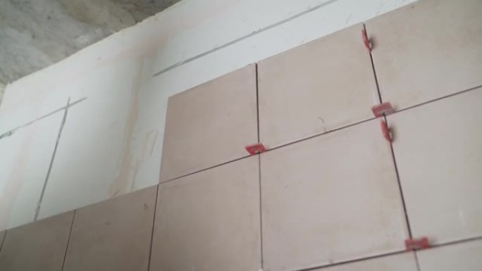 浴室里的一块小瓷砖。在墙上铺瓷砖。工业工人，杂工在浴室墙壁上安装小瓷砖
