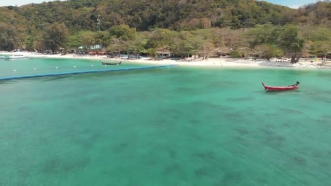 田园诗般的香蕉海滩湾，带有浮码头平台和停泊在泰国Koh Hey (珊瑚岛) 翡翠水域上的乡村渔船-空