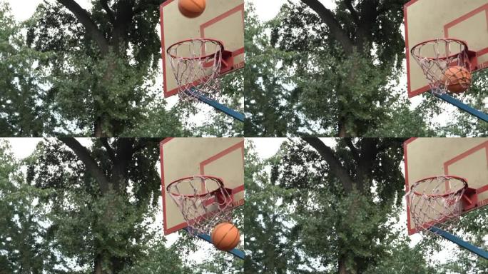 投掷的橙色篮球在树荫下的室外球场上击中了篮筐。击中目标。达到目标