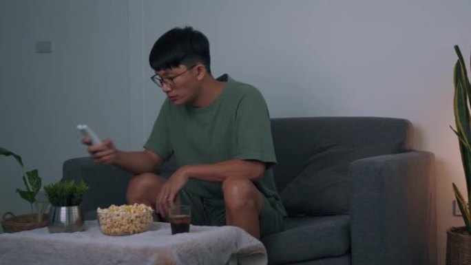 亚洲男子晚上在客厅看连续剧，一边吃爆米花。