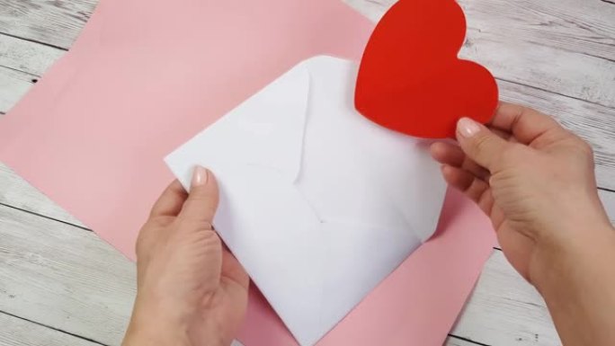 女人双手将一张红色心形的情人卡放在白色的信封中，向情人节快乐或特别的生日庆祝活动表白