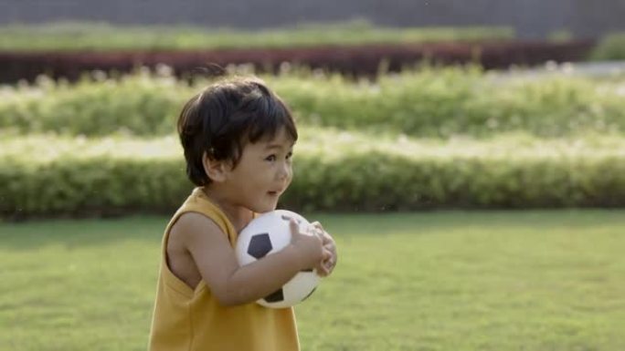 亚洲小男孩穿着黄色衬衫，在草坪中央踢足球。