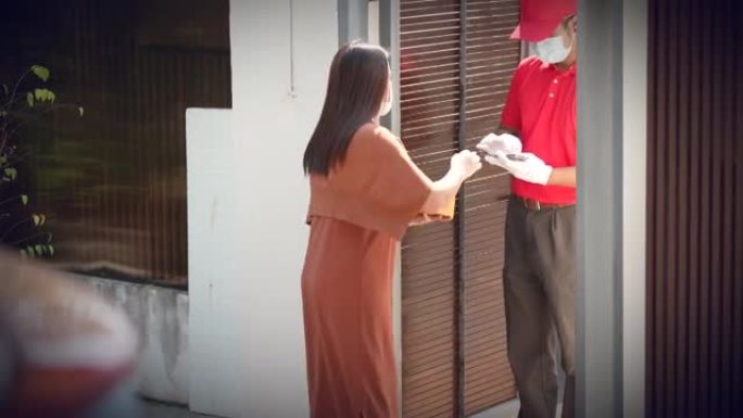 家庭送货服务在covid19期间，亚洲送货男子戴着红色制服的口罩在家送货给顾客。网上购物概念。