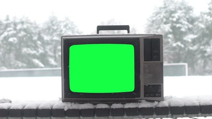 冬季长椅上绿屏的老式电视被雪覆盖