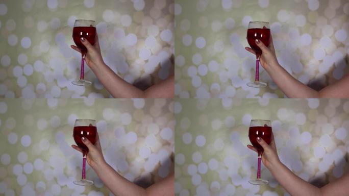一个女人的手在闪闪发光的背景上拿着一杯玫瑰酒