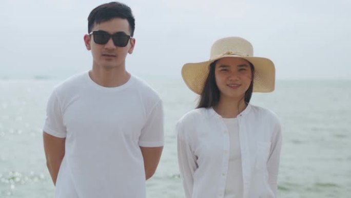 微笑的肖像夫妇站在海边看着相机，享受暑假，开心地说笑。旅行情侣概念。