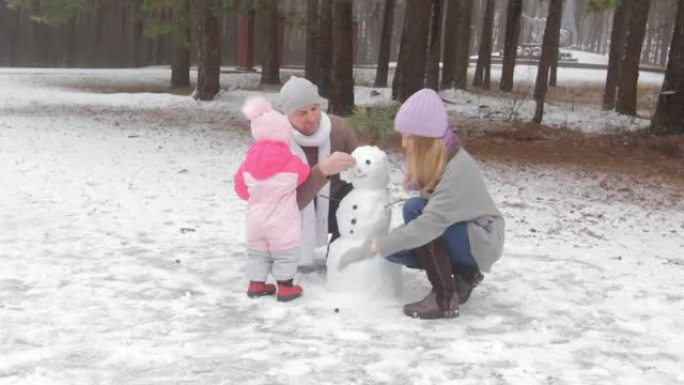 一对幸福的夫妇和一个小孩在冬季森林里堆雪人