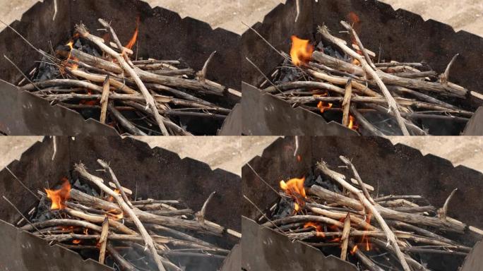 燃烧的柴树枝特写火。露天燃烧篝火。野餐。烧烤。人的手把柴树枝扔进火的火中。火焰的舌头。