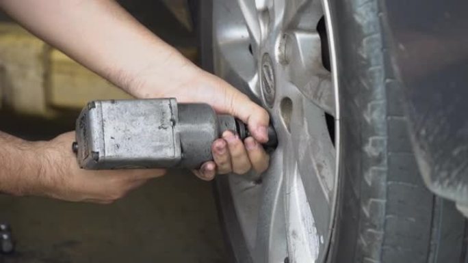 在汽车维修车库的车间里，在汽车上使用气动扳手或冲击扳手更换轮的机械师