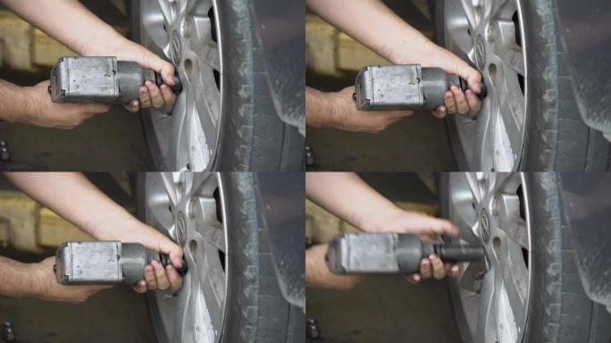 在汽车维修车库的车间里，在汽车上使用气动扳手或冲击扳手更换轮的机械师