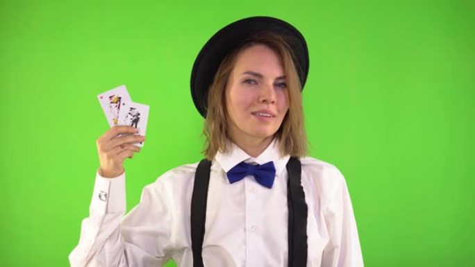 穿着白衬衫和帽子的副主持人展示了扑克牌，微笑着眨眨眼。小丑卡。绿屏，工作室，色度键