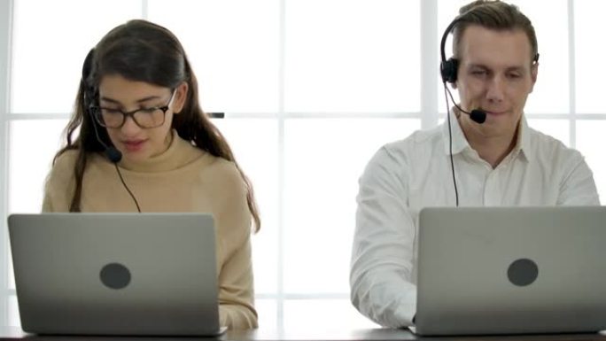 年轻的男女呼叫中心戴着耳机与笔记本电脑一起工作，同时咨询有在线问题的客户。