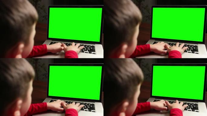 坐在桌子旁的男孩用绿色色度键在笔记本电脑上打字的视图