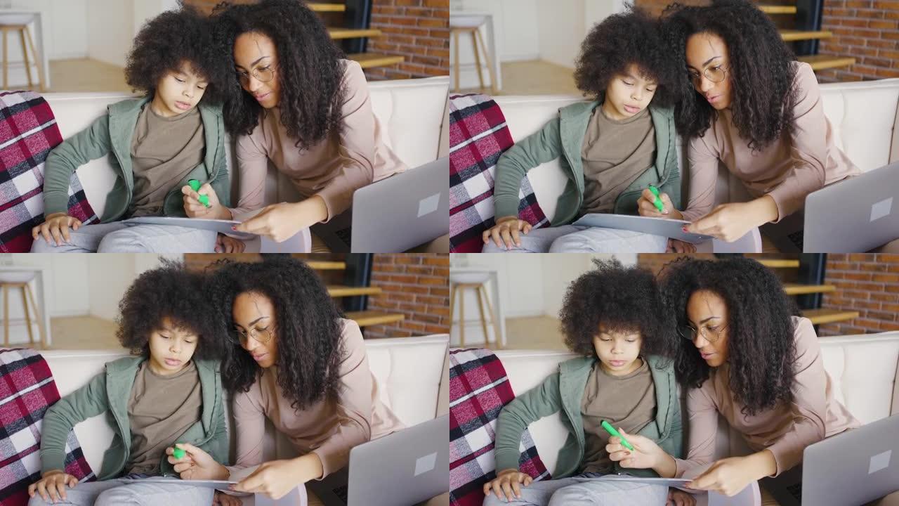 非裔美国母亲和儿子在使用笔记本电脑时画画。卷曲的黑发女人和孩子在家里有扇子的肖像。呆在家里