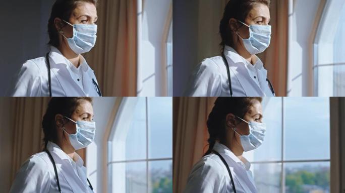 戴着防护口罩的成熟美女在办公室休息一下，她透过医院的窗户看着全景