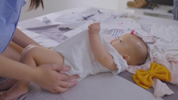 女孩宝宝在睡布上看着妈妈一起玩耍的动作的侧视图，一个5个月可爱的宝贝女儿躺在卧室的床上，亚洲家庭在早