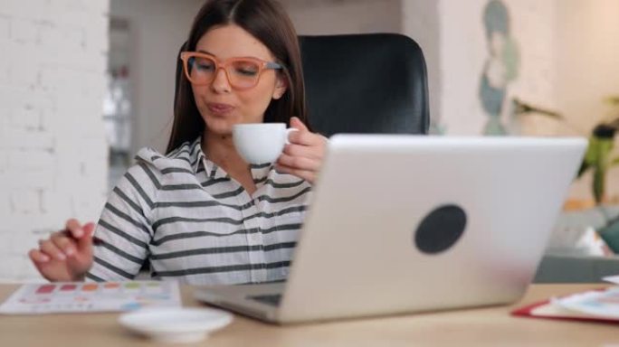 年轻的女商人在办公桌前工作时喝咖啡。她正在分析财务报告，并准备提高业务收入的新方法。