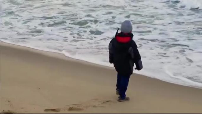 一个非常活跃的孩子在冬天在海滩上玩耍