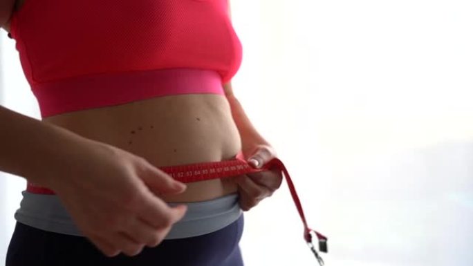 女孩用卷尺测量腰围。运动负荷，减肥饮食，产后体重恢复
