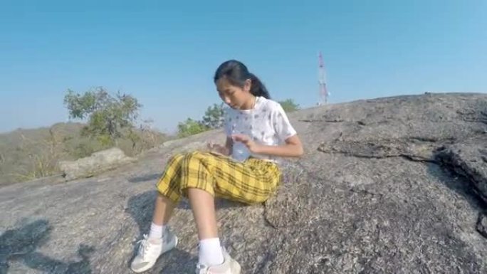 快乐的亚洲女孩使用数字平板电脑，而坐在山上的视点在早上，生活方式的概念。