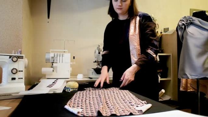 在她的工作室里为切割新衣服的女性时装设计师铺展面料。在创意设计工作室工作。服装新集合的概念。