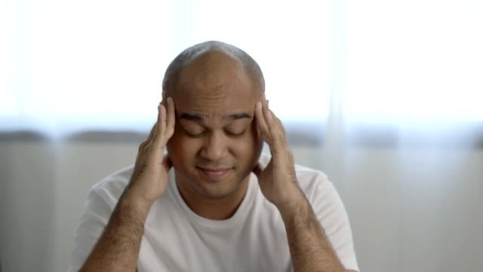 穿着白色t恤的30岁左右的亚洲秃头男人睡不好觉。他背部疼痛，颈部疼痛，无法入睡。